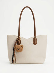 Cream slouch tote bag with brown handles and teddy bear charm, front view