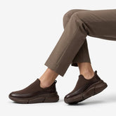 Brown stretch knit slip-on sneakers worn with taupe trousers