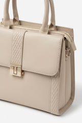Angled close-up of cream satchel showing T-bar clasp and embossed panel