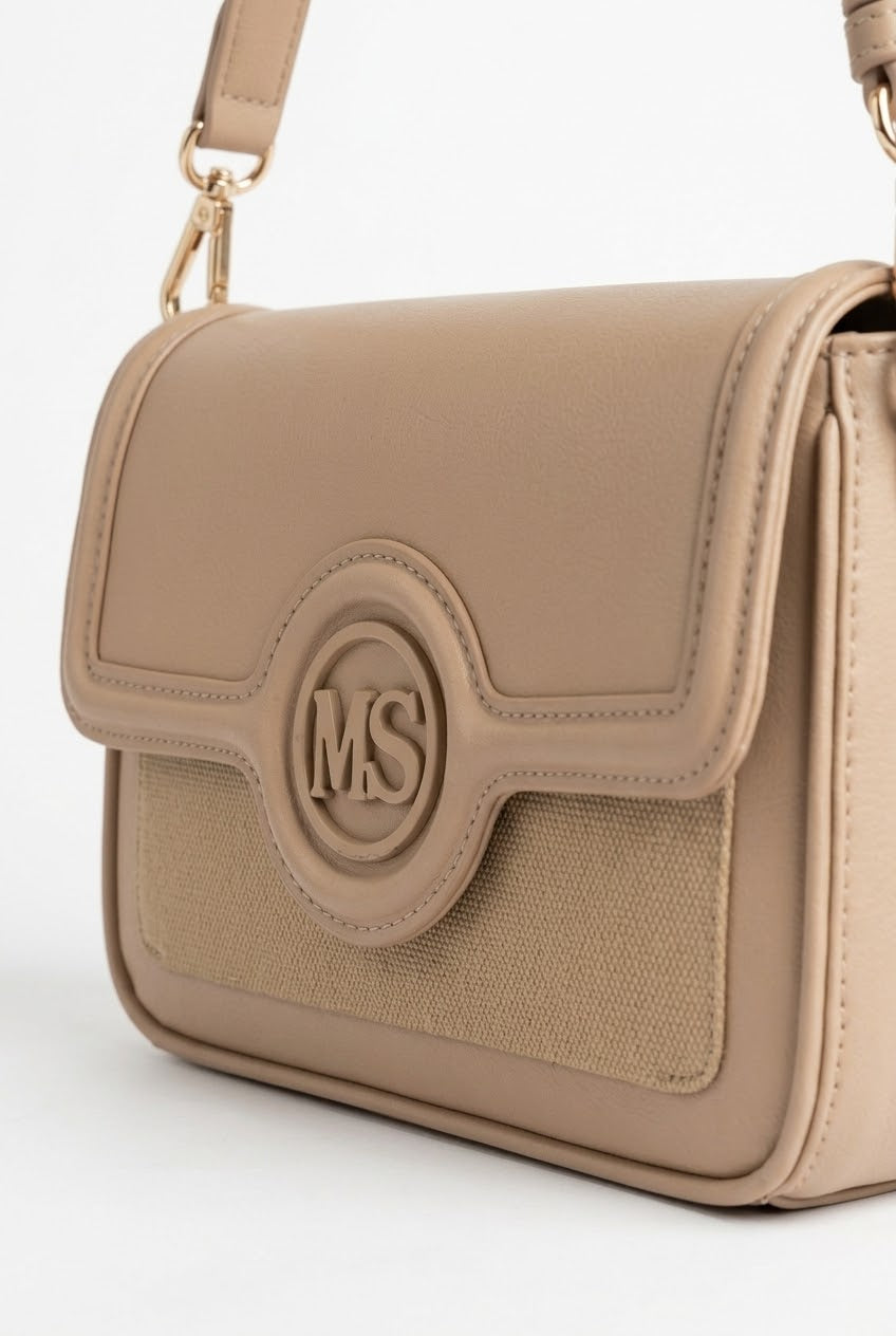 Close-up of tan flap bag showing monogram medallion and woven panel