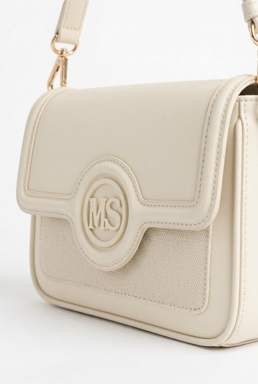 Close-up of cream flap bag showing monogram medallion and woven texture