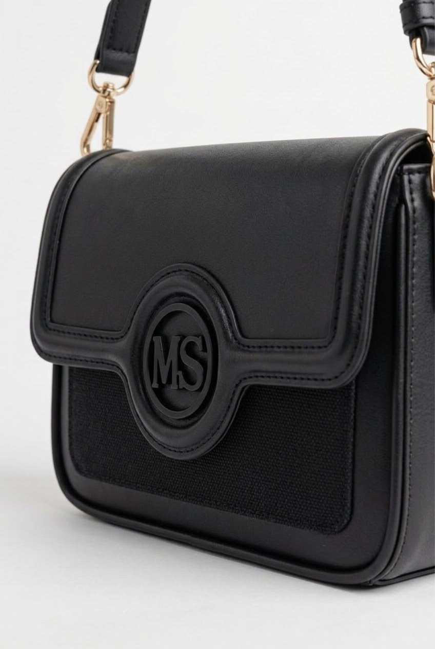 Close-up of black flap bag showing monogram medallion and woven panel