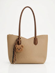 Tan slouch tote bag with brown handles and teddy bear charm, front view